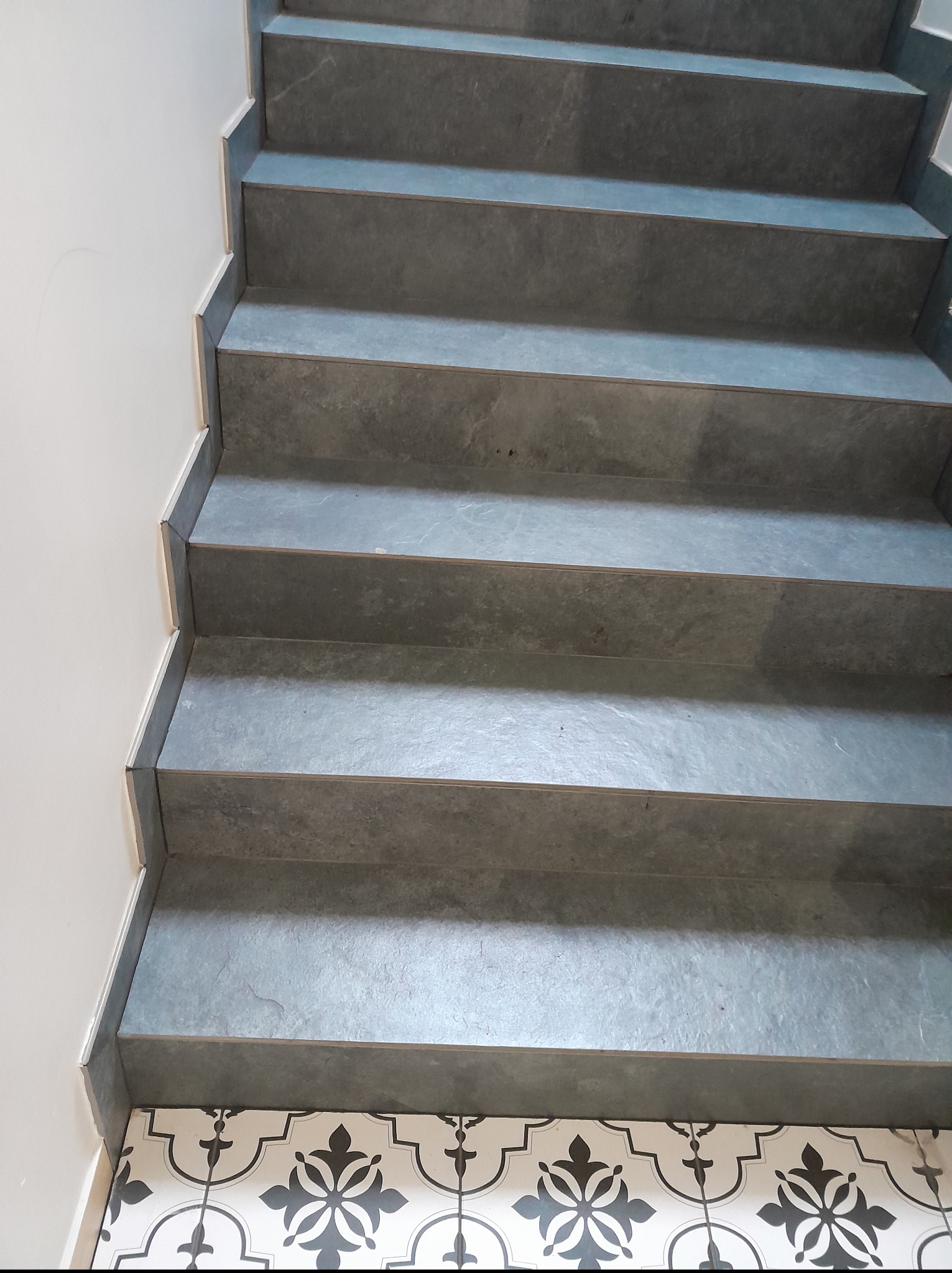 Wykończone schody z szarymi płytkami, widok z góry. U dołu dekoracyjna podłoga w biało-czarne wzory. Estetyczne połączenie materiałów i kolorów, schludne wykonanie.