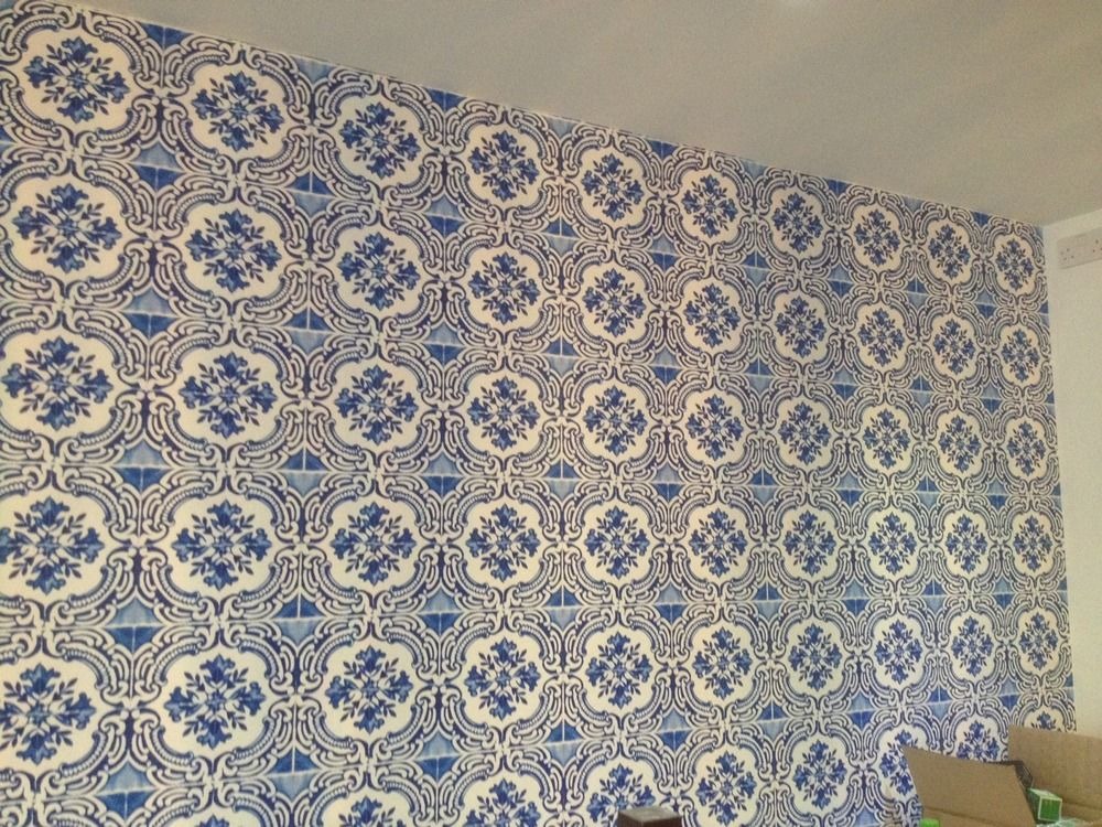 Ściana wyłożona dekoracyjnymi, kwadratowymi płytkami ceramicznymi w odcieniach bieli i niebieskiego, tworzącymi wzór kwiatowy. Widok na fragment pokoju.