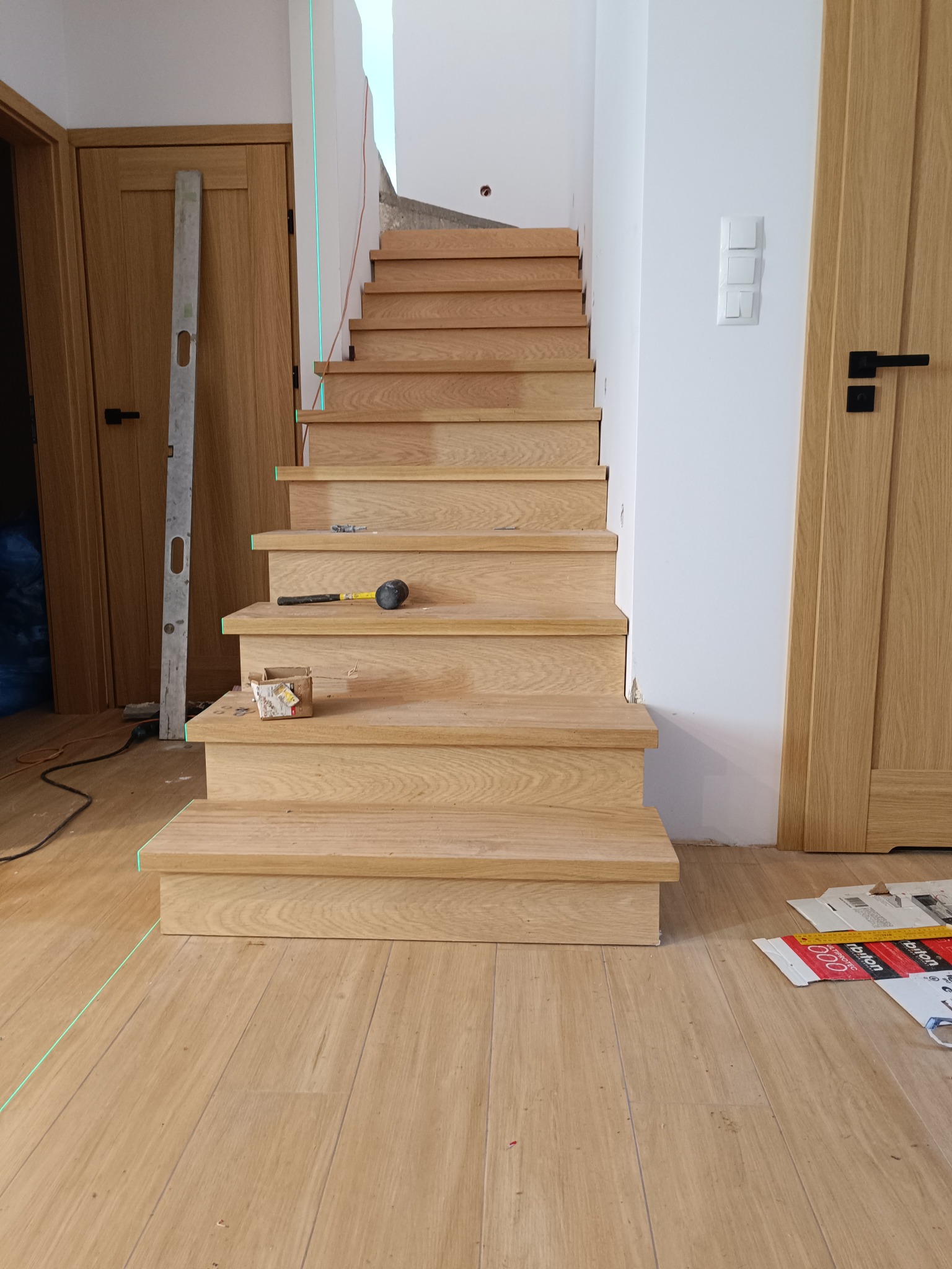 Montaż drewnianych schodów z poziomnicą i narzędziami. Widoczne detale wykończenia, jasne drewno i białe ściany. Ujęcie z dołu, podkreślające perspektywę schodów.