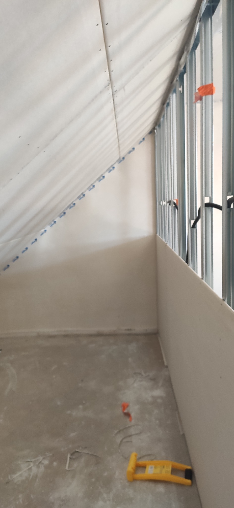 Skośne poddasze w trakcie zabudowy płytami gipsowo-kartonowymi, widoczne metalowe profile i narzędzia na podłodze. Ujęcie z dołu, surowy stan wykończenia.