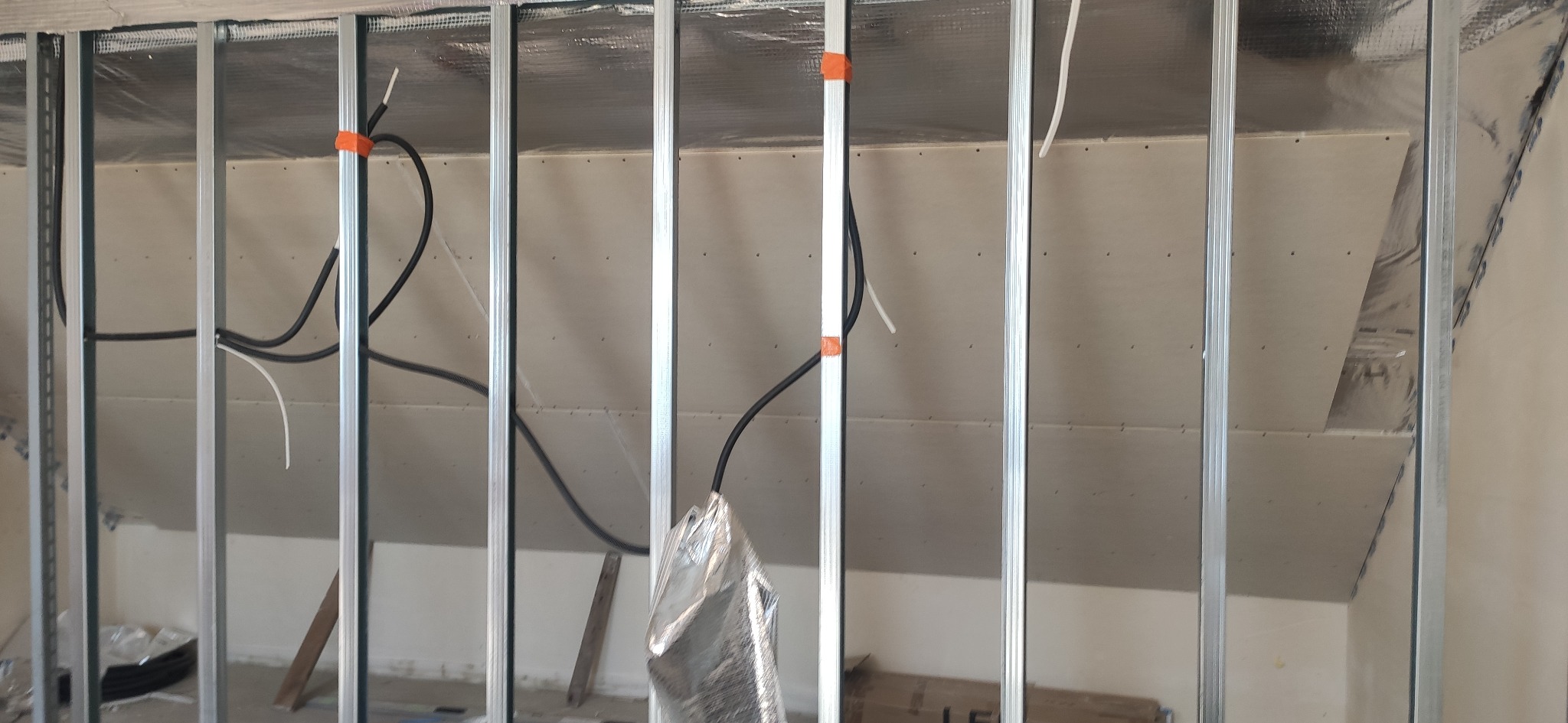 Metalowa konstrukcja ścianki działowej z płyt gipsowo-kartonowych, widoczne przewody elektryczne. Etap prac wykończeniowych w pomieszczeniu ze skosem.