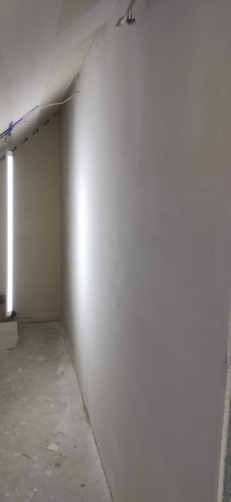 Wygładzona ściana w Oławie po szpachlowaniu, gotowa do malowania. Widoczne ślady po taśmie malarskiej i oświetlenie budowlane.