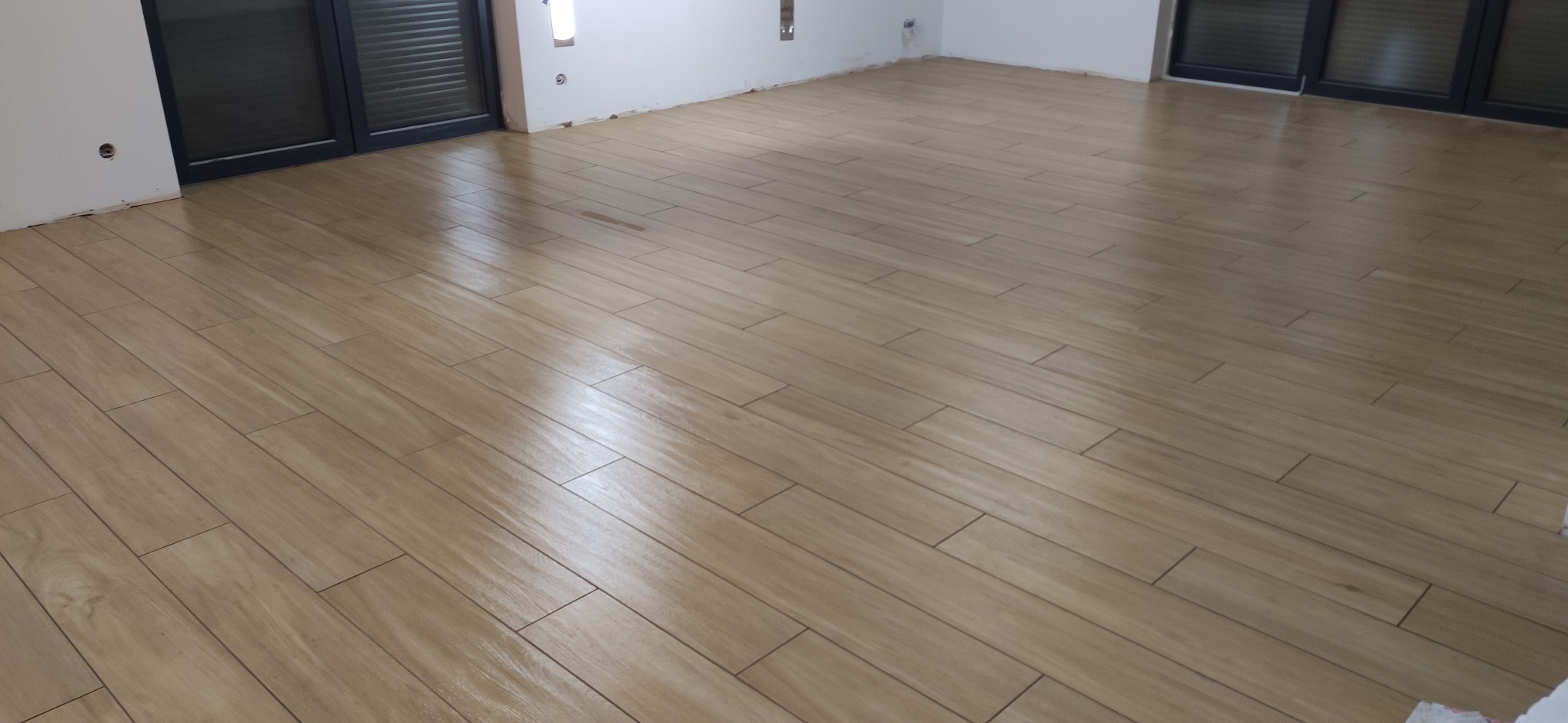 Ułożona podłoga z płytek imitujących drewno w jasnym odcieniu, widok z góry, świeżo po montażu, z widocznymi fragmentami ścian i okien.