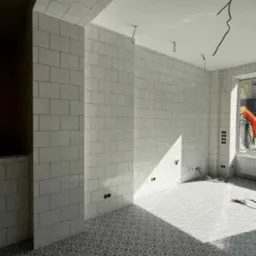 Wykończona łazienka z białymi płytkami na ścianach i wzorzystą podłogą. Widoczne gniazdka elektryczne i instalacje pod oświetlenie.