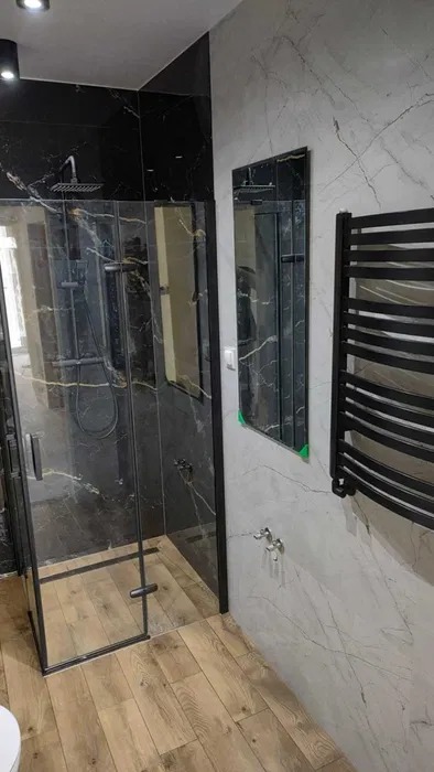 Nowoczesna kabina prysznicowa z czarnymi elementami i imitacją marmuru w Kielcach, uzupełniona o lustro i grzejnik drabinkowy.