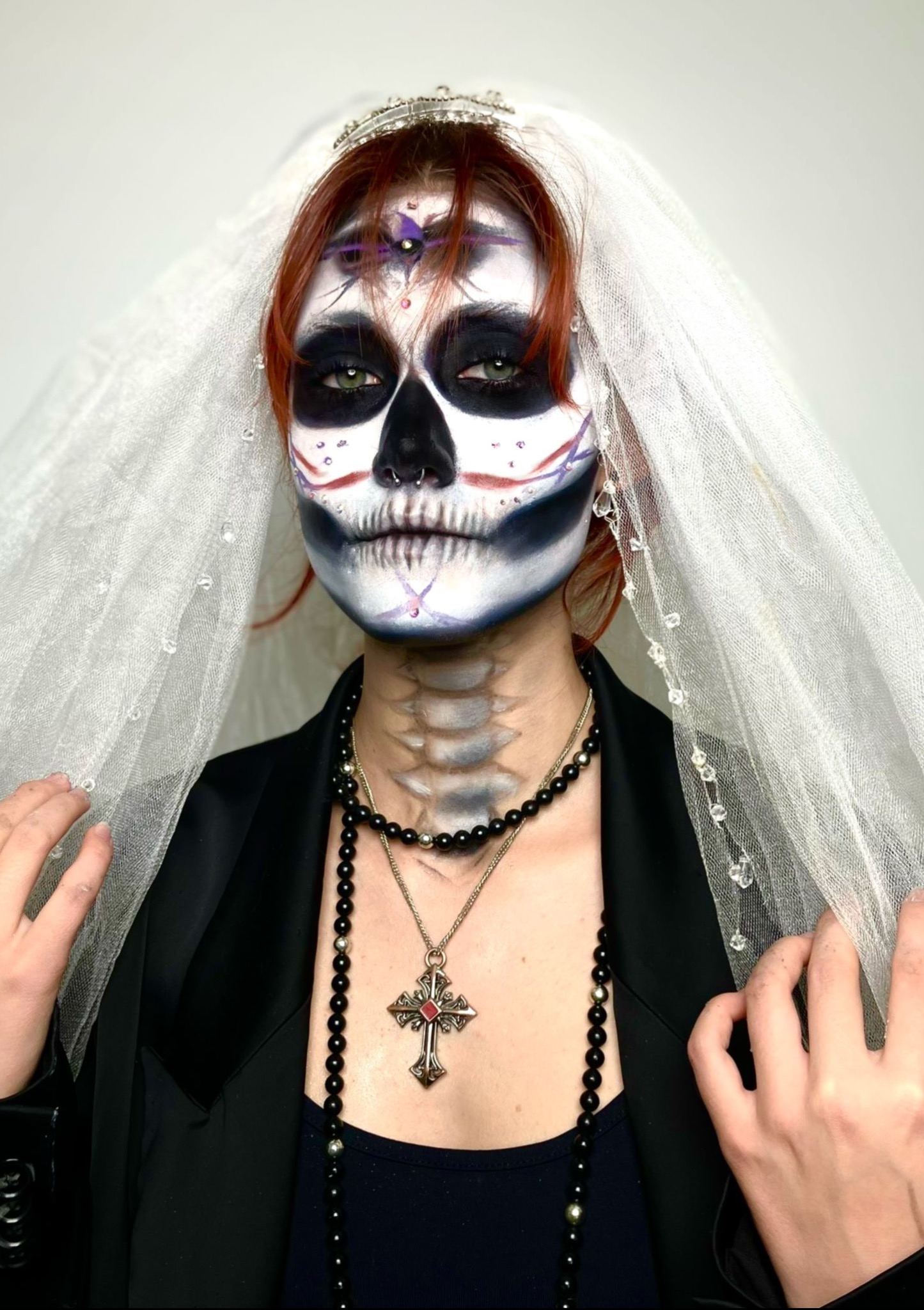 Kobieta z artystycznym makijażem inspirowanym motywem czaszki, w welonie i czarnej marynarce, pozuje na jasnym tle. Halloween.