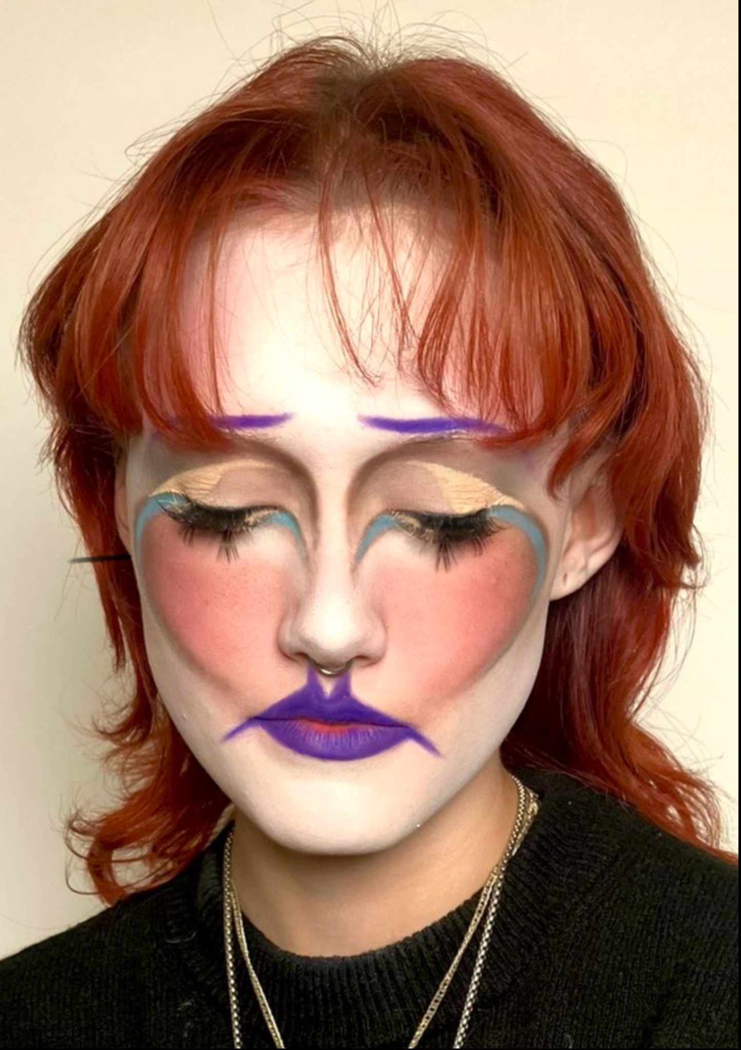 Artystyczny makijaż z purpurowymi ustami i sercami na policzkach, uzupełniony o niebieskie akcenty i mocno podkreślone rzęsy na tle jasnej karnacji i rudych włosów.
