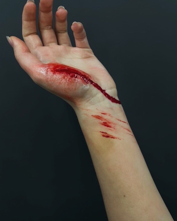 Realistyczny makijaż FX: głęboka rana na przedramieniu z efektem krwi, wykonana przez wizażystę. Widoczne detale i tekstura skóry.