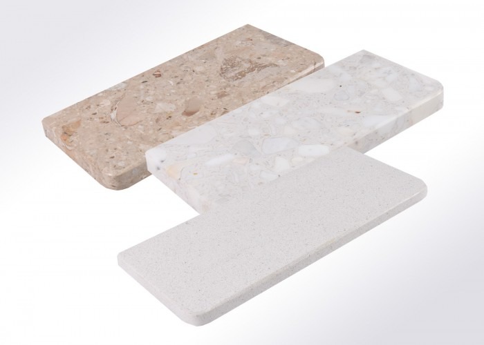 Trzy próbki blatów kamiennych o różnych fakturach i kolorach: beżowy trawertyn, biały lastryko i szary kwarcyt, ułożone ukośnie na białym tle.