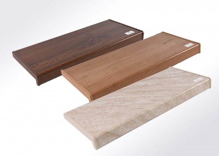 Trzy parapety o różnej fakturze (drewno, marmur) i kolorystyce, ułożone ukośnie na jasnym tle. Widoczne detale wykończenia krawędzi.