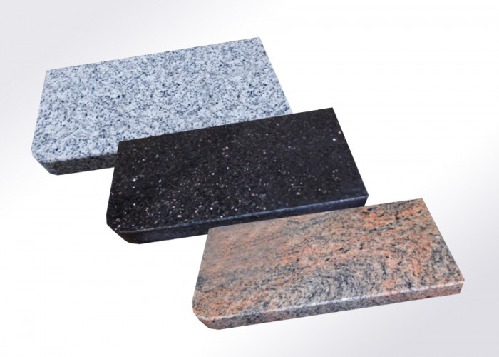 Trzy próbki blatów kamiennych: szary granit, czarny z brokatem i różowo-szary marmur, zaokrąglone krawędzie, gładka powierzchnia, jednolite tło.