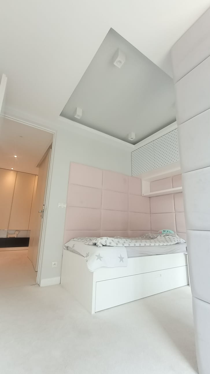 Jasne wnętrze pokoju dziecięcego z łóżkiem z szufladami, panelem tapicerowanym w odcieniach różu i oświetleniem punktowym. Minimalistyczny design, świeżo po remoncie.