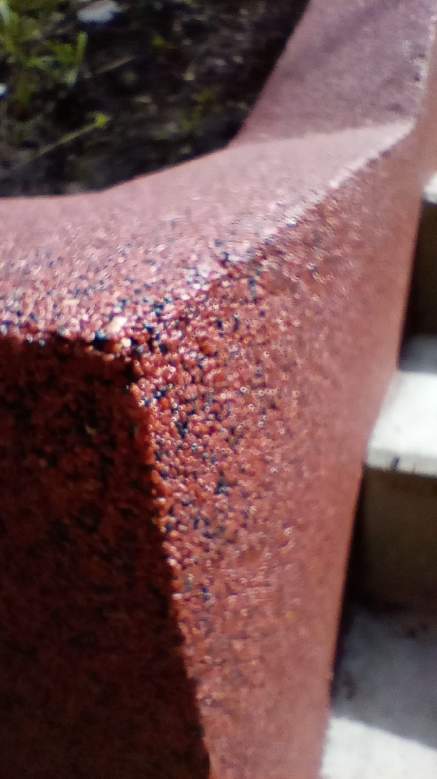 Zbliżenie na pomalowany element architektoniczny w odcieniach czerwieni z wyraźną fakturą, widoczne schody w tle. Detal wykończenia z bliska.