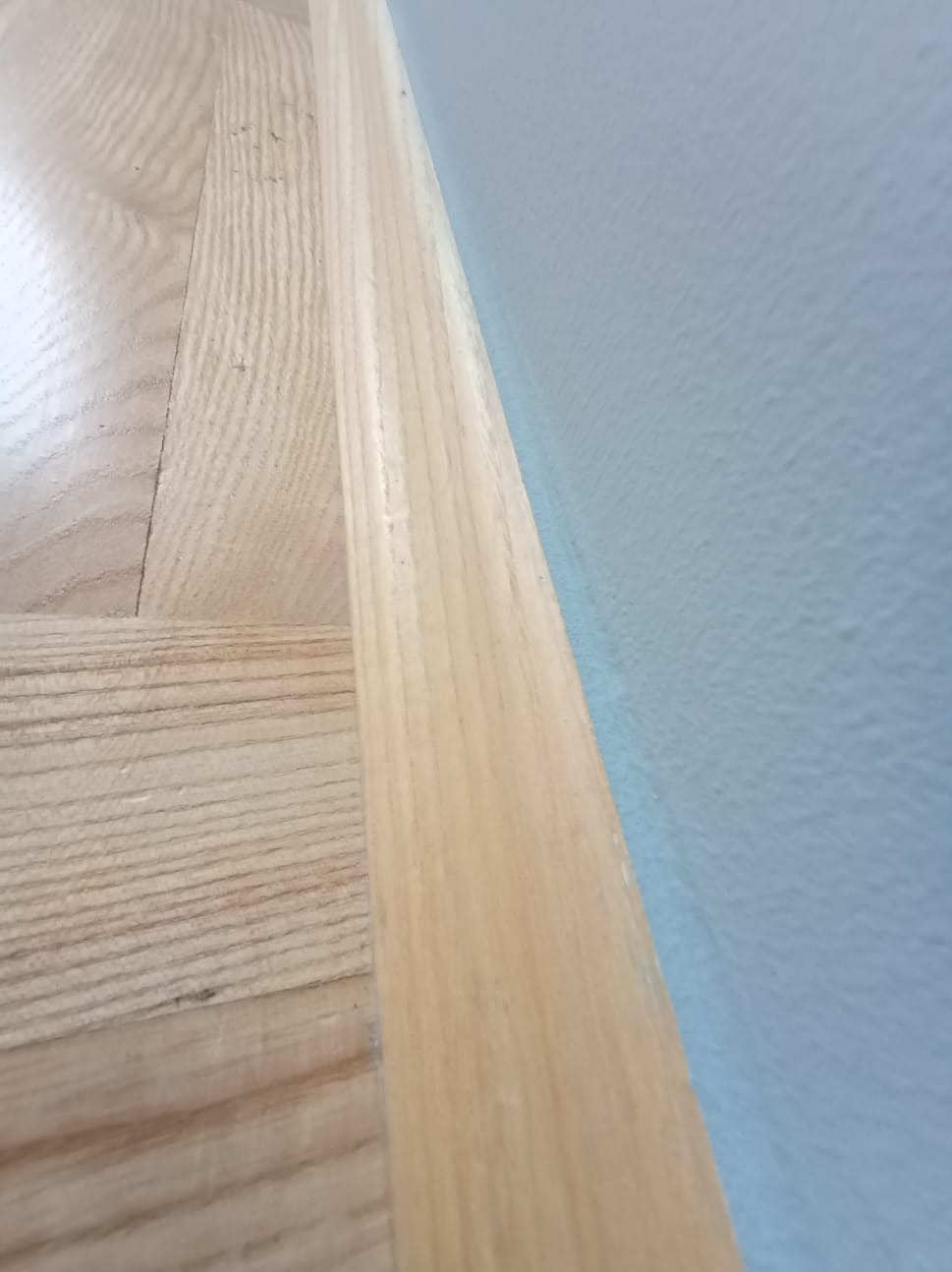 Fragment wykończonego wnętrza: drewniana podłoga z listwą przypodłogową i pomalowana na jasny niebieski kolor ściana z widoczną fakturą. Ujęcie z bliska.