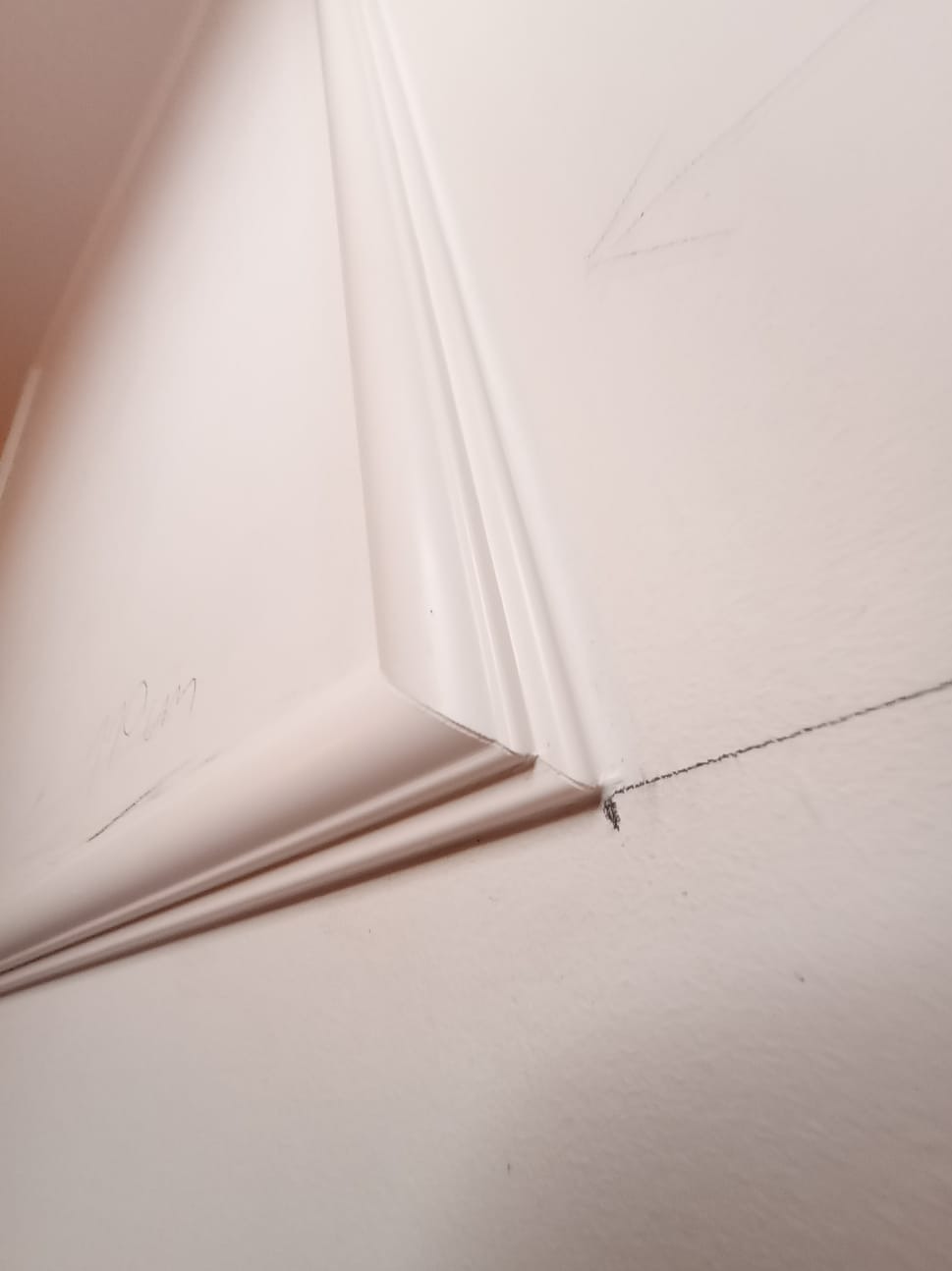 Biała listwa przypodłogowa zamontowana na ścianie, widoczne ślady ołówka i niedoskonałości powierzchni przed malowaniem. Ujęcie z dołu, bliski kadr.