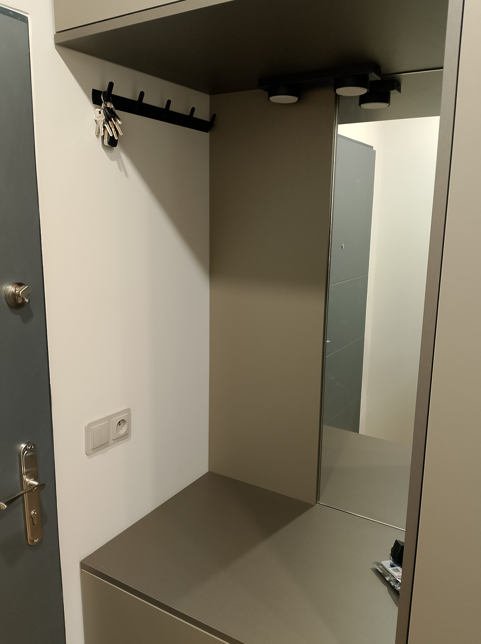 Nowoczesna szafka z lustrem i wieszakiem na klucze w przedpokoju, szara kolorystyka, minimalizm.