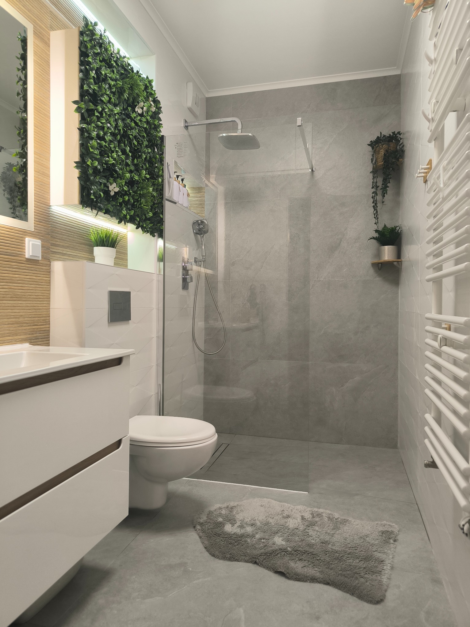 Nowoczesna łazienka z kabiną typu walk-in, umywalką z szafką i pionową zieloną ścianą. Szare płytki imitujące kamień i białe elementy wyposażenia.