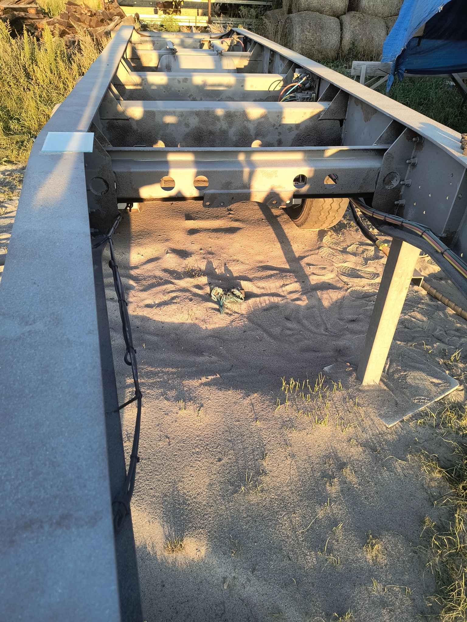 Metalowa rama przyczepy po piaskowaniu, z widocznymi śladami obróbki i elementami konstrukcyjnymi. W tle bele siana.