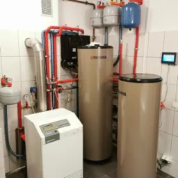 Kompletna kotłownia: dwa bojlery Technix, biały piec Supastar, czarny moduł sterujący, naczynia przeponowe i rury w pomieszczeniu wyłożonym płytkami.