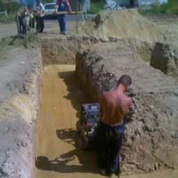Wykopy pod fundamenty domu jednorodzinnego, pracownicy przy wykopie, ubijarka wibracyjna do zagęszczania gruntu.