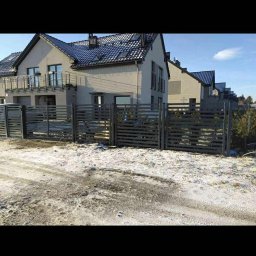 Kamil Aszyk K.G.J.W - Nowoczesne, poziome ogrodzenie posesji z szarego drewna, widoczne na tle domów jednorodzinnych w Pelplin. Śnieżny krajobraz, błękitne niebo.