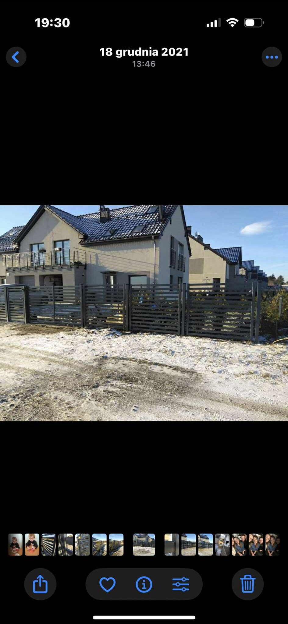 Nowoczesne, poziome ogrodzenie posesji z szarego drewna, widoczne na tle domów jednorodzinnych w Pelplin. Śnieżny krajobraz, błękitne niebo.