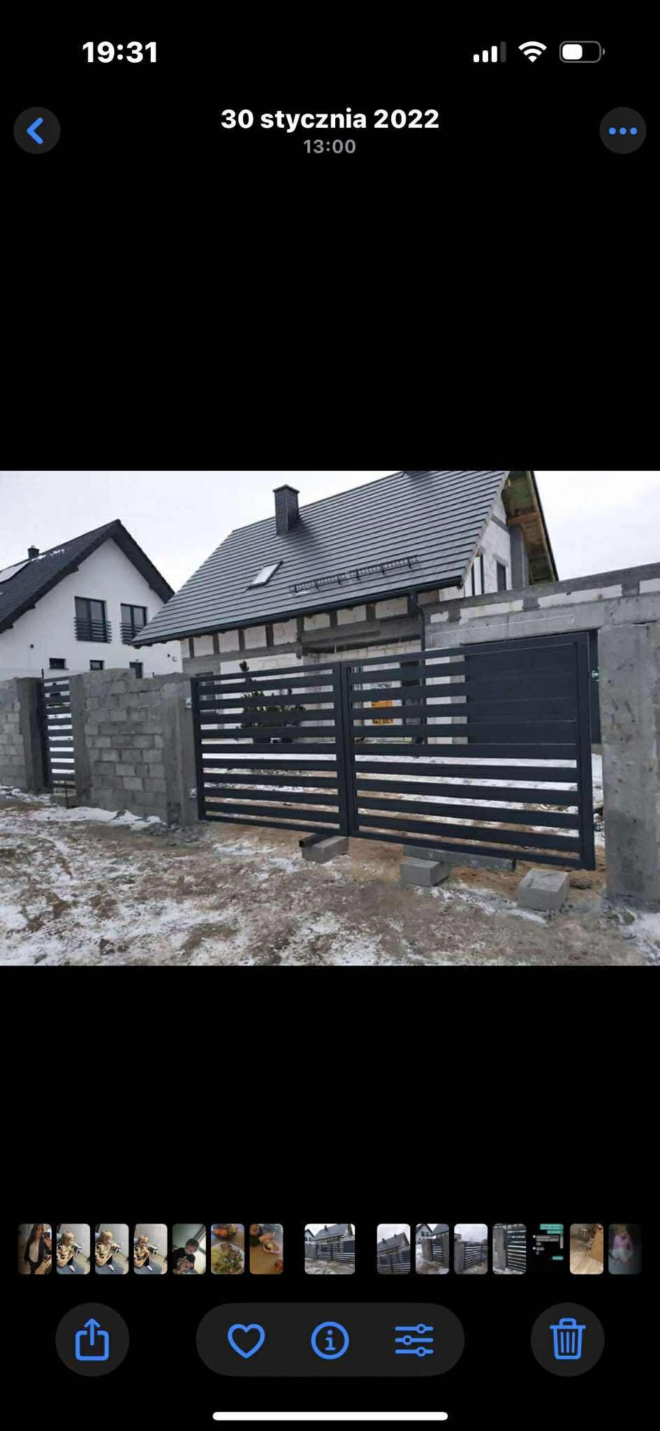 Nowoczesna, pozioma brama wjazdowa z metalowymi panelami, osadzona w surowych, betonowych słupkach. Tło stanowi budynek w trakcie budowy, zimowy krajobraz.