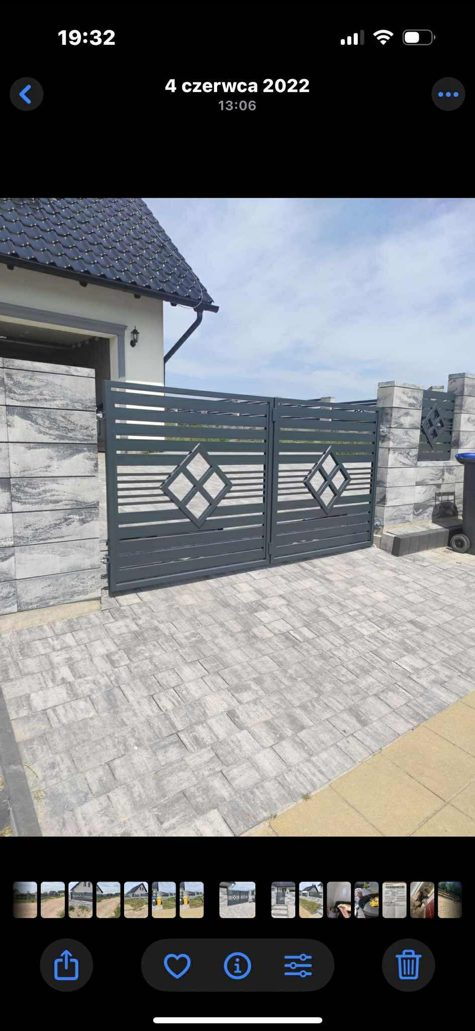 Nowoczesna, grafitowa brama wjazdowa z poziomymi szczeblami i romboidalnym wzorem na tle domu z szarą kostką brukową. Słupki bramy z tego samego materiału.