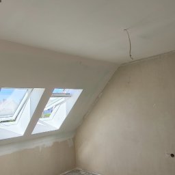 filar-BUD - Pokój na poddaszu po szpachlowaniu ścian i sufitu, widoczne okna dachowe, sufit z siatką przygotowany do dalszych prac wykończeniowych.