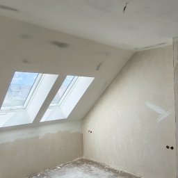 filar-BUD - Pokój na poddaszu w trakcie prac wykończeniowych: ściany po szpachlowaniu, widoczne trzy okna dachowe, podłoże przygotowane do dalszych prac.