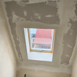 filar-BUD - Poddasze w trakcie prac wykończeniowych: ściany i sufit po szpachlowaniu, widoczne okno dachowe i rusztowanie. Etap przygotowania do malowania.