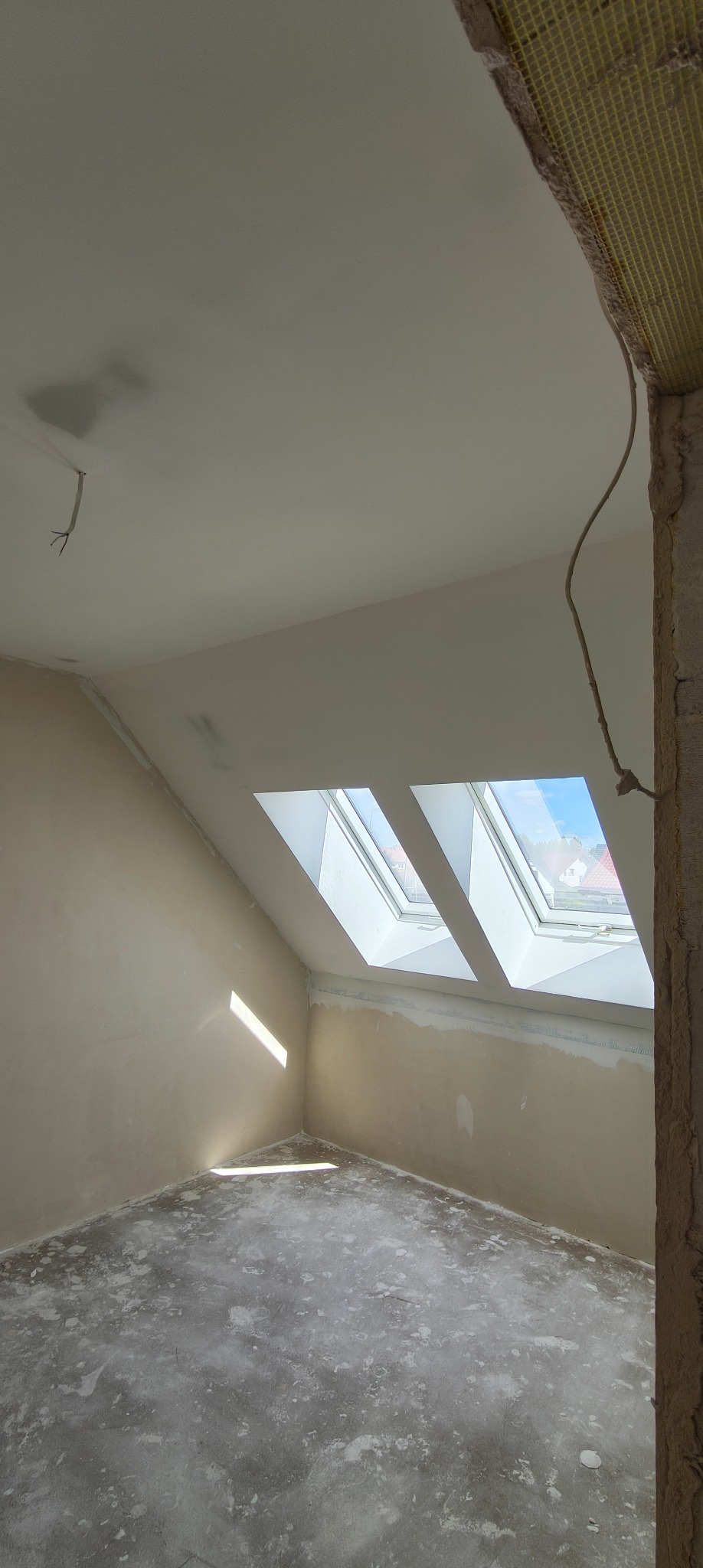 Pokój na poddaszu w trakcie prac wykończeniowych. Widoczne okna dachowe, ściany przygotowane pod malowanie i surowa podłoga.