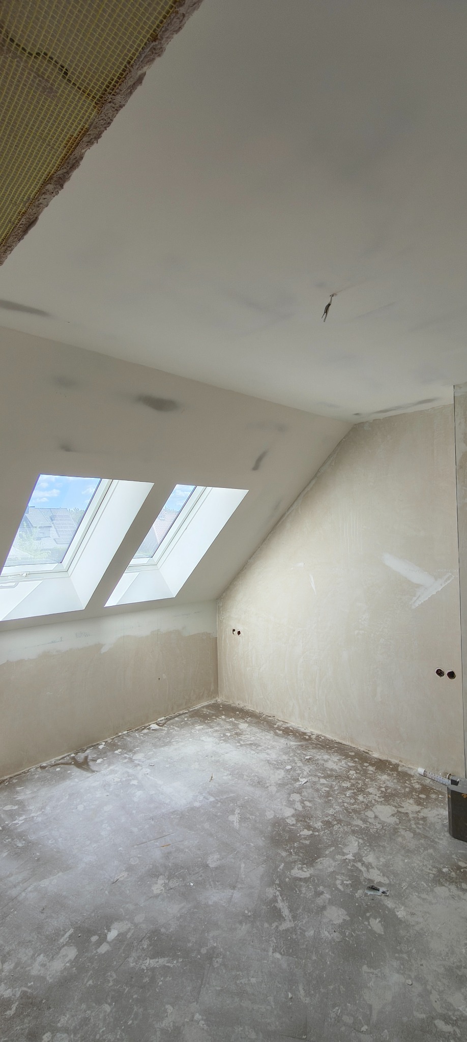 Pokój na poddaszu w trakcie prac wykończeniowych: ściany po szpachlowaniu, widoczne trzy okna dachowe, podłoże przygotowane do dalszych prac.