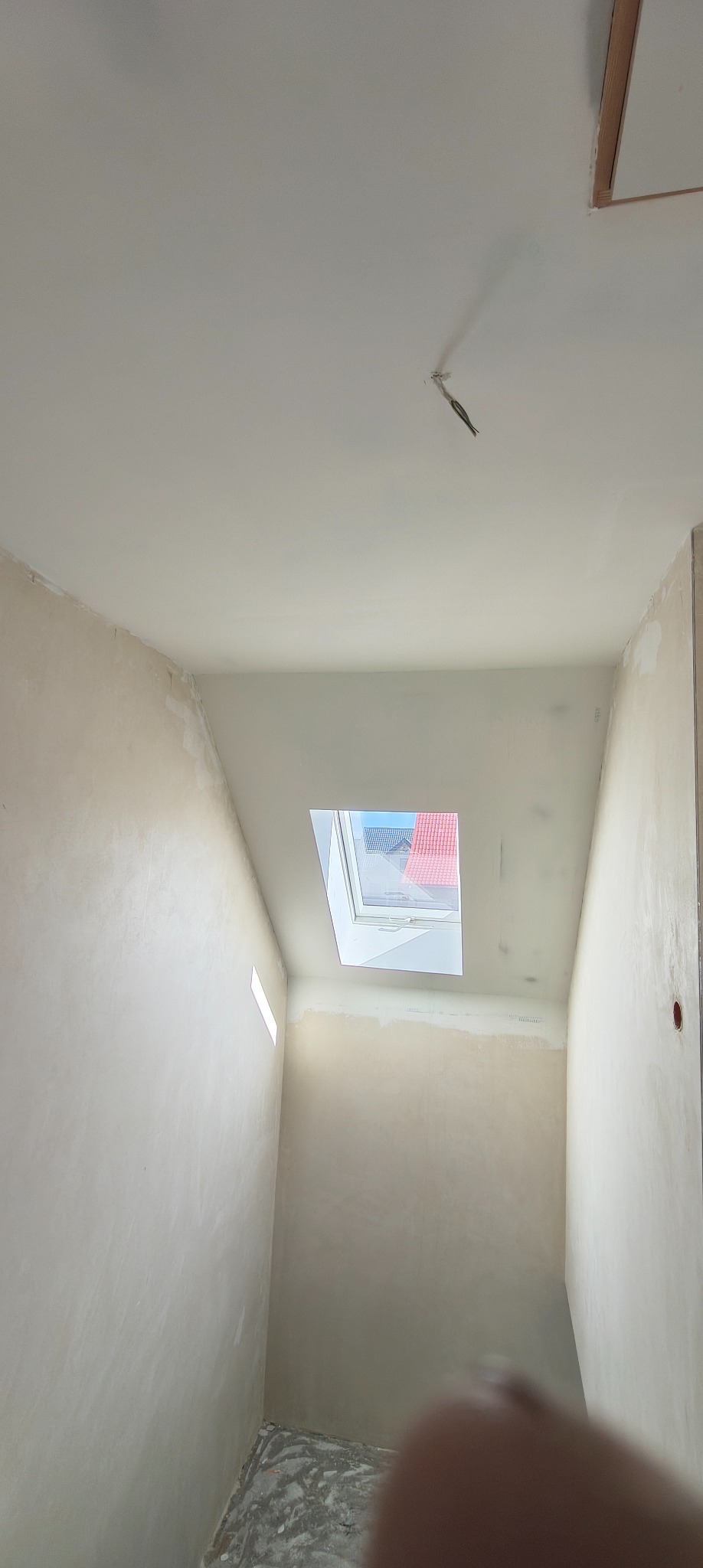 Wnętrze w trakcie prac wykończeniowych: ściany po szpachlowaniu, widoczne okno dachowe. Fragment instalacji elektrycznej wystaje z sufitu.