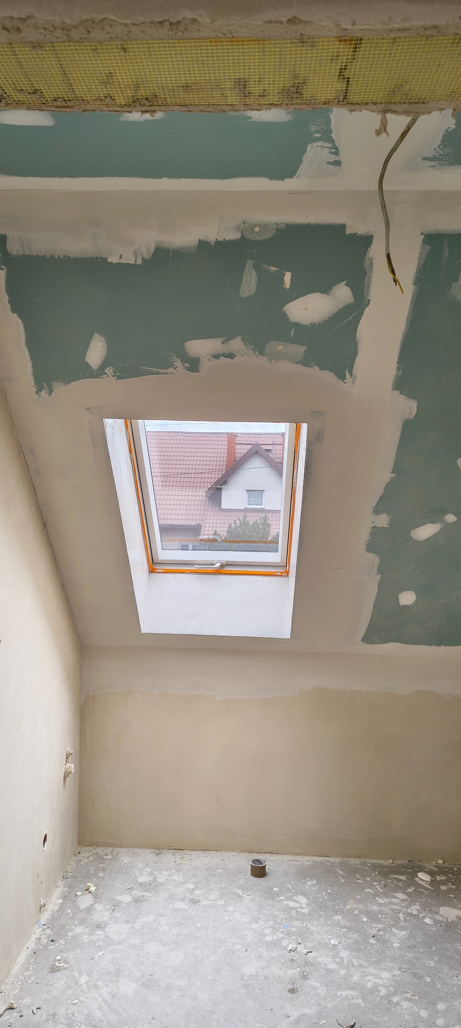 Pokój na poddaszu w trakcie prac wykończeniowych: ściany przygotowane pod malowanie, okno dachowe, widoczna siatka na suficie.