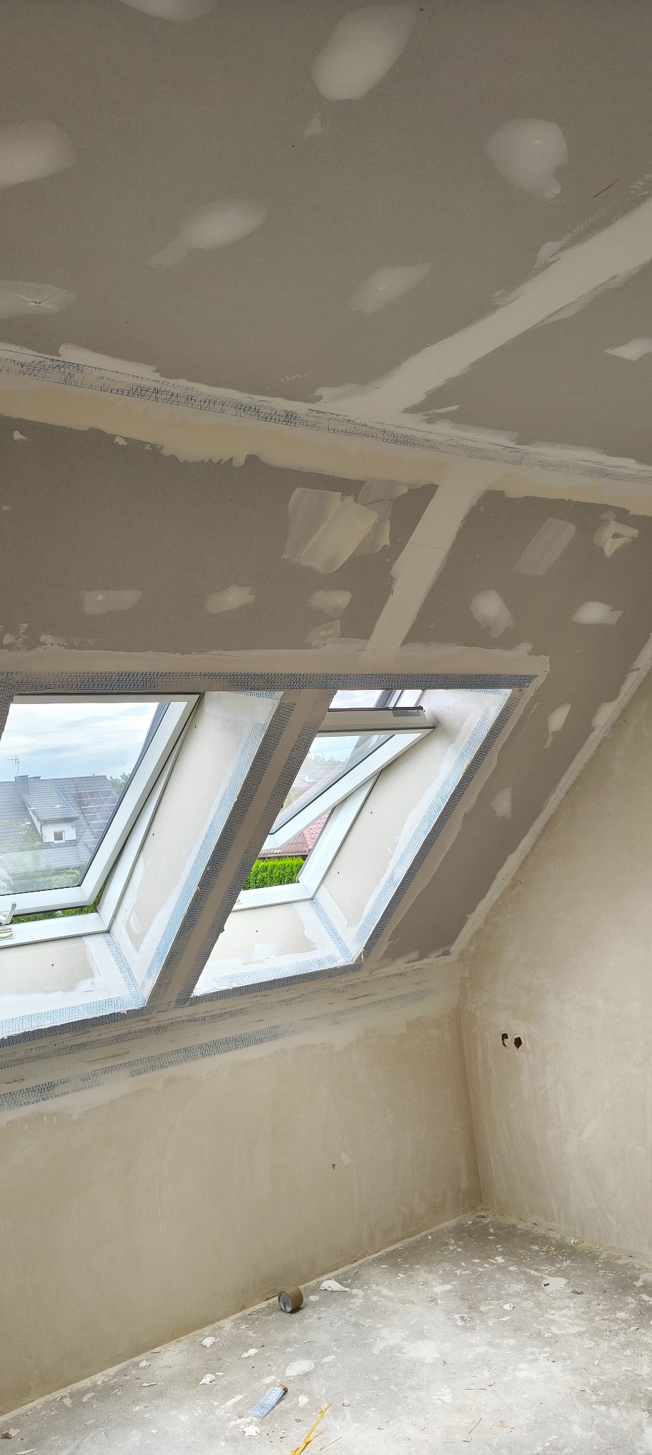 Poddasze ze skośnym oknem dachowym w trakcie prac. Widoczne płyty kartonowo-gipsowe z siatką wzmacniającą na łączeniach, częściowo wyszpachlowane.