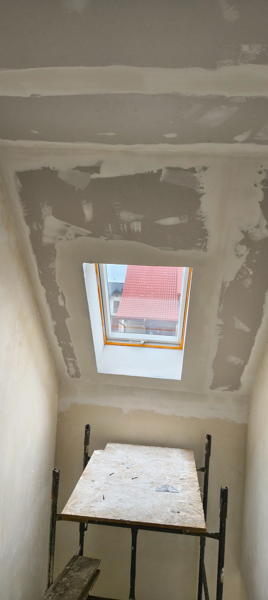 Poddasze w trakcie prac wykończeniowych: ściany i sufit po szpachlowaniu, widoczne okno dachowe i rusztowanie. Etap przygotowania do malowania.