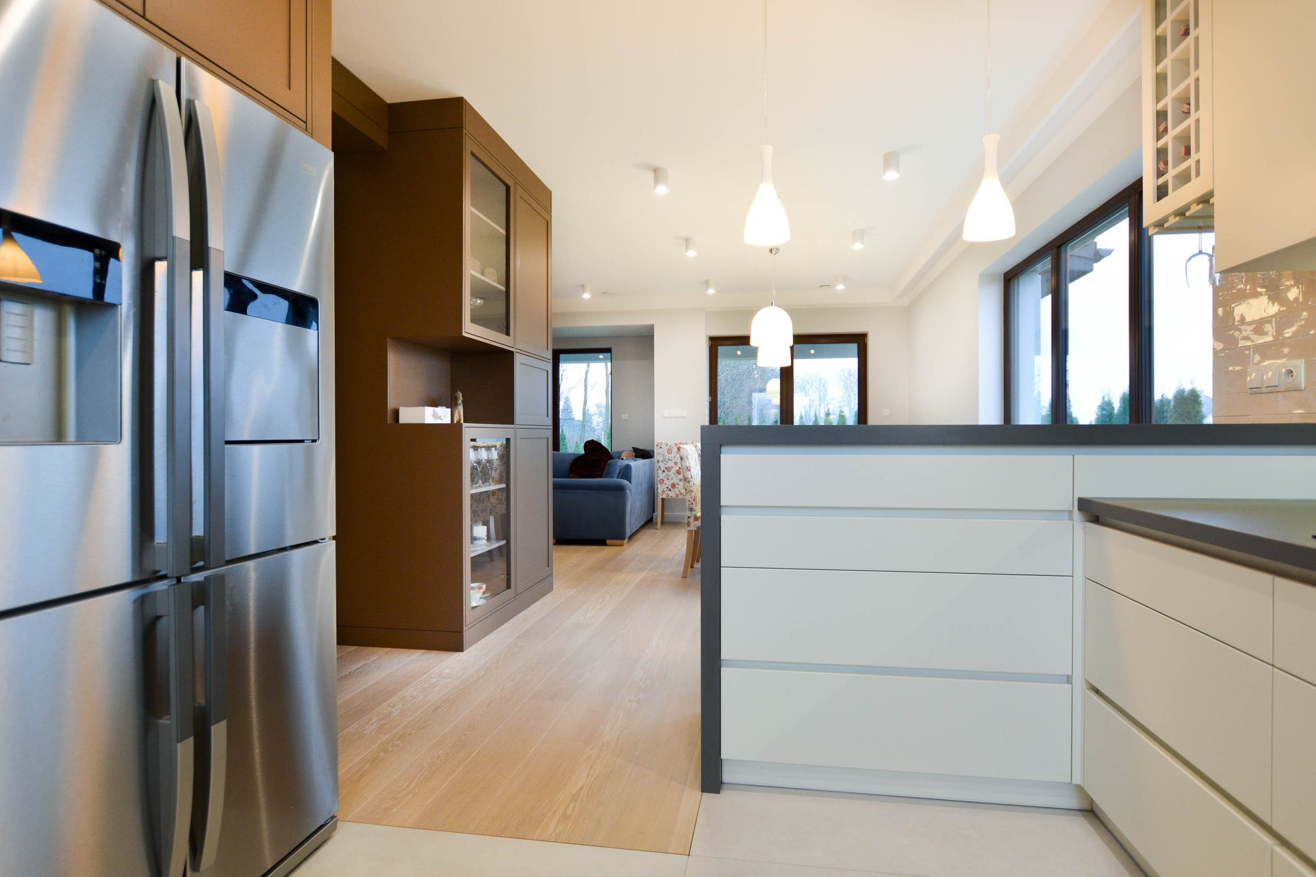 Nowoczesna kuchnia z wyspą i dużym, srebrnym lodówko-zamrażarką w Lublinie. Widok na salon z niebieską sofą i duże okna.