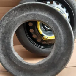 Koło zapasowe Goodyear na stalowej feldze, z piankowym wypełnieniem. Widok z bliska na tle kartonowej powierzchni.