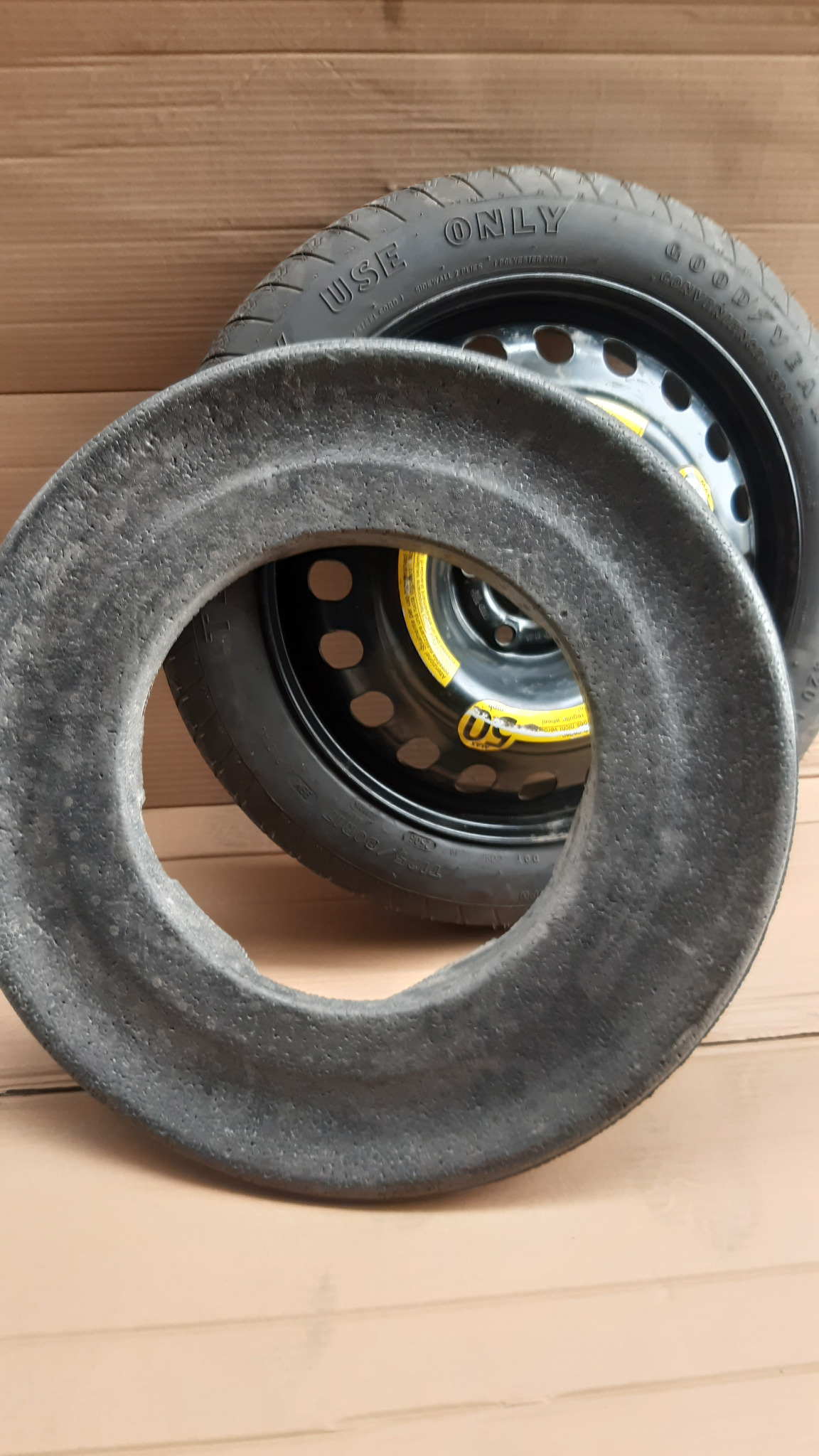 Koło zapasowe Goodyear na stalowej feldze, z piankowym wypełnieniem. Widok z bliska na tle kartonowej powierzchni.