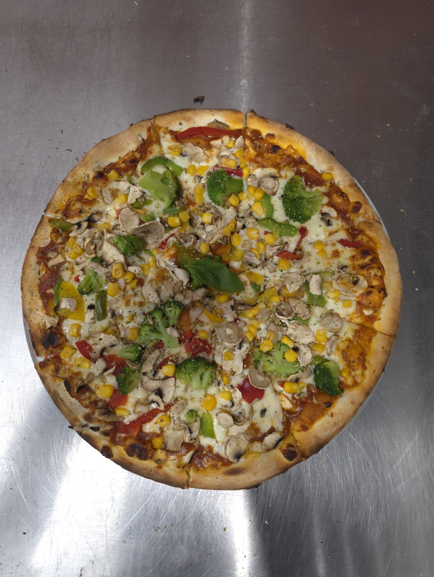 Okazała pizza wegetariańska z brokułami, kukurydzą, pieczarkami i papryką na metalowym blacie, idealna na catering imprezowy.