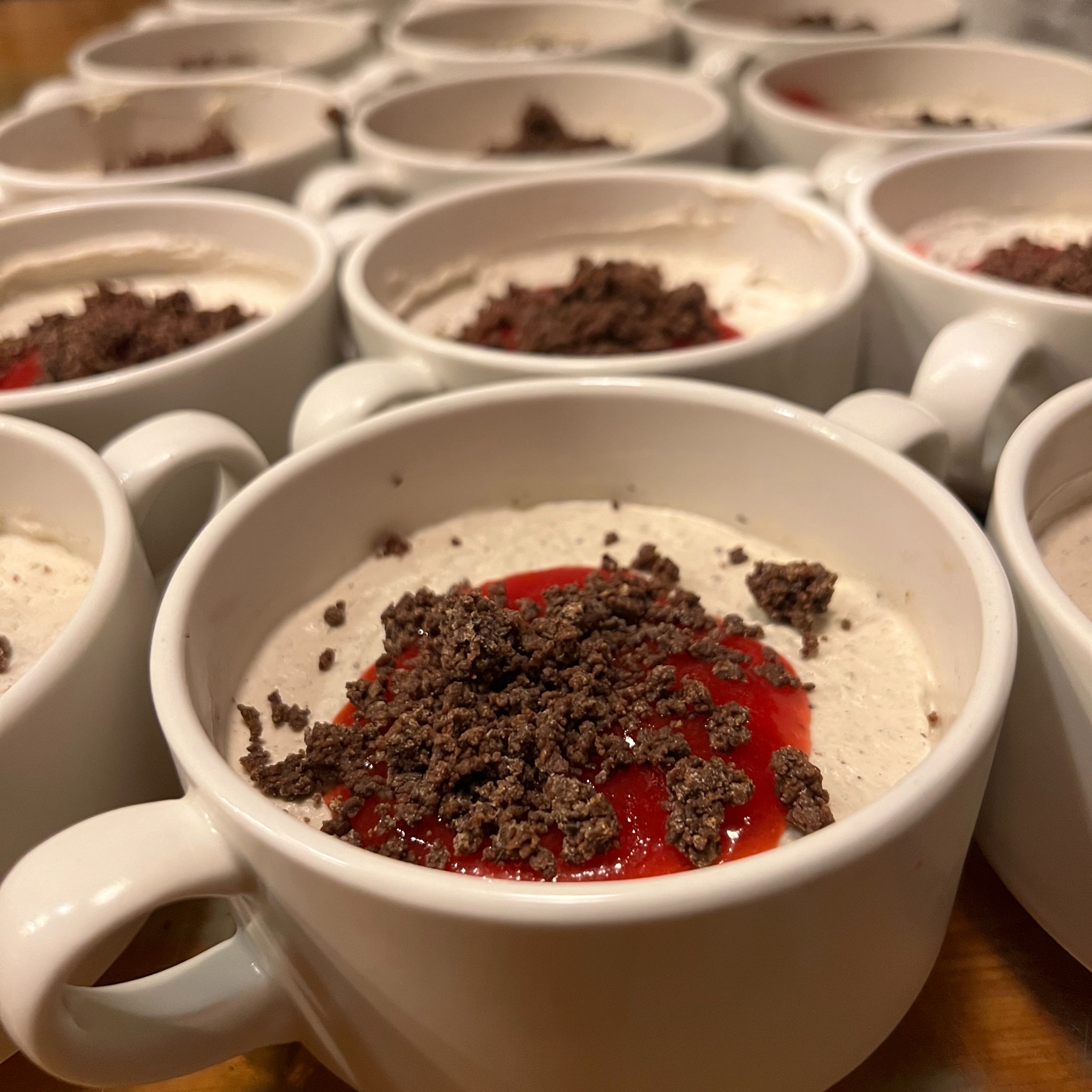 Deser w białych filiżankach: krem, czerwony sos i posypka czekoladowa. Catering na imprezę, słodki poczęstunek z bliska, widok z góry.