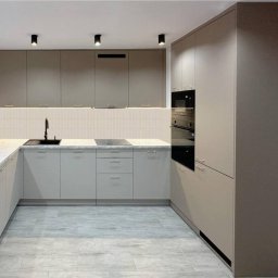 OL MEBLE SPÓŁKA Z OGRANICZONĄ ODPOWIEDZIALNOŚCIĄ - Jasna kuchnia z marmurowym blatem i czarną armaturą. Górne szafki w kolorze taupe, dolne szaro-beżowe. Nad blatem białe płytki z subtelnym wzorem.