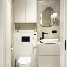 Nowoczesna łazienka w beżach: podwieszana toaleta, umywalka nablatowa z szafką, lustro o nieregularnym kształcie i szafka wisząca. Minimalistyczny design.