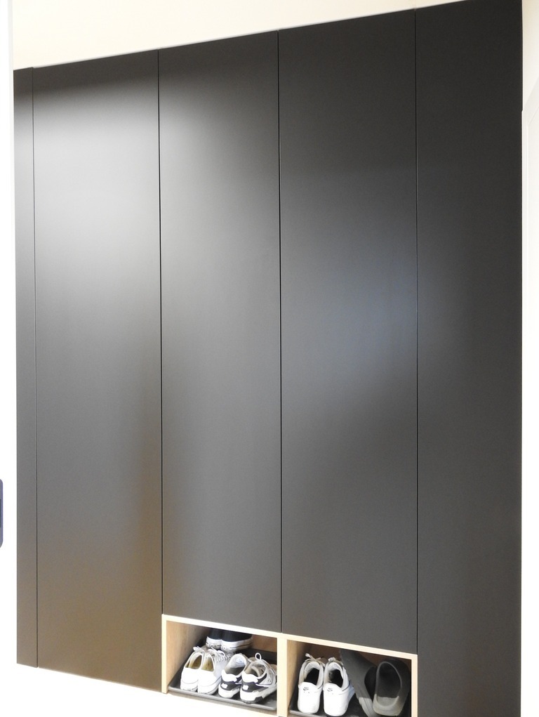 Czarna, matowa szafa wnękowa z otwartymi półkami na buty w dolnej części. Minimalistyczny design, jasne tło, widoczne obuwie.