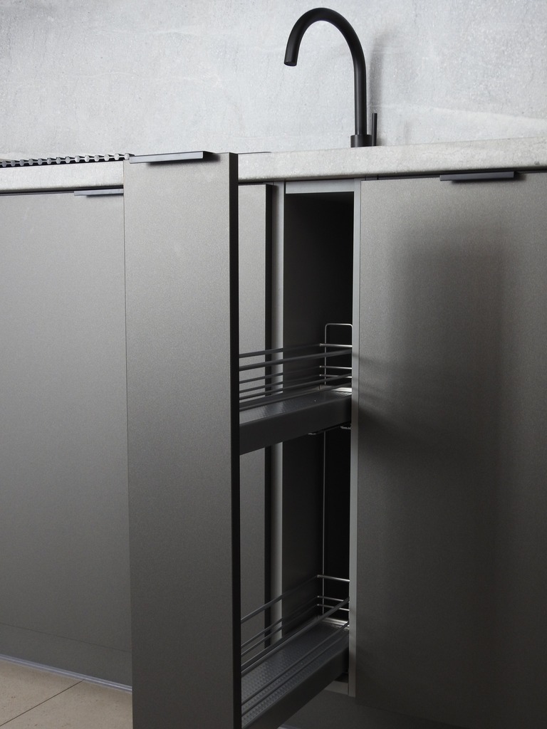 Szara, nowoczesna zabudowa kuchenna z wysuwanymi koszami cargo i czarną baterią. Minimalistyczny design, gładkie fronty, subtelne uchwyty.