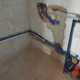 Instalacja rur wodnych w surowym wnętrzu. Widoczne fragmenty ścian z betonu komórkowego i ślady po kuciu. Częściowo zamontowany stelaż podtynkowy.