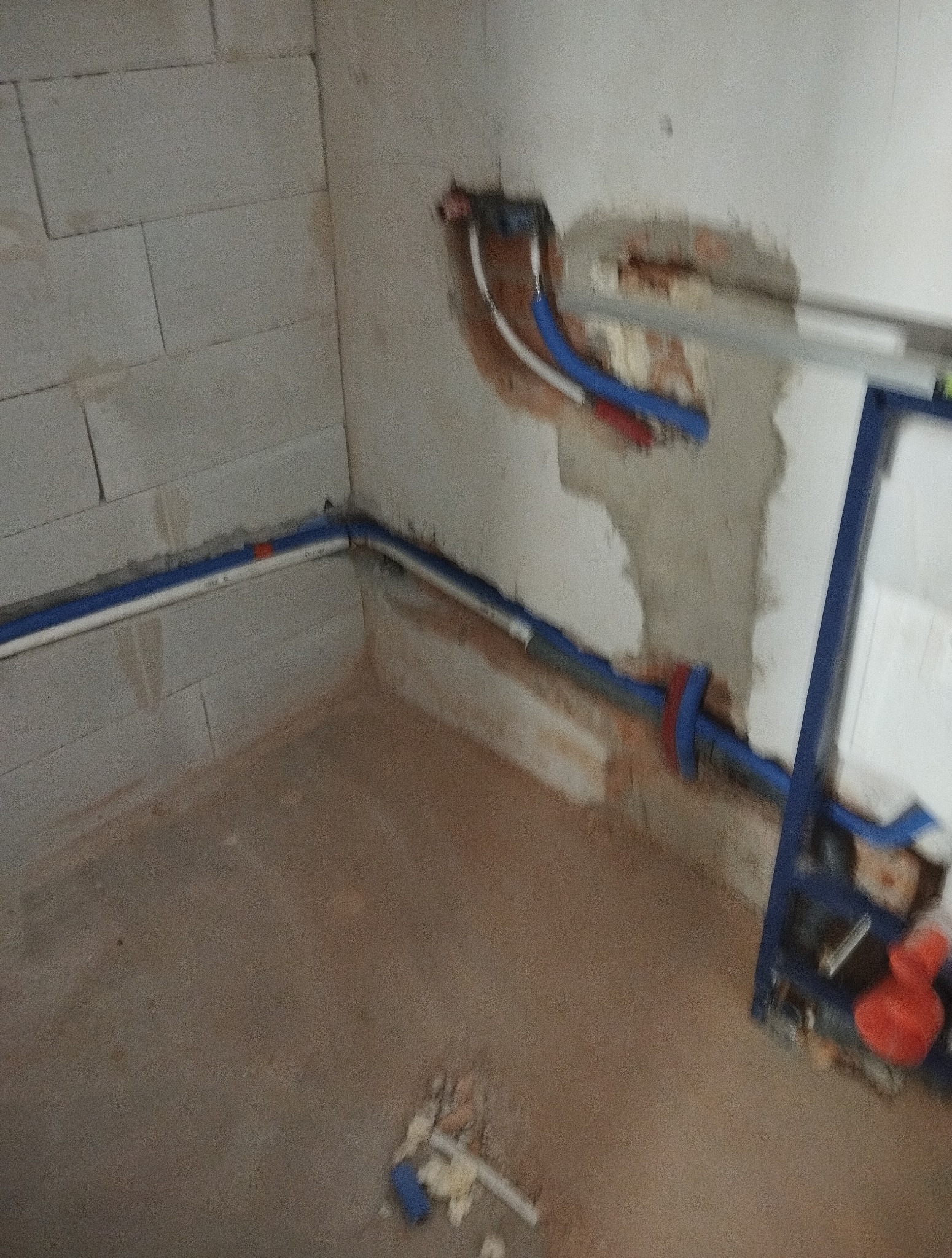 Instalacja rur wodnych w surowym wnętrzu. Widoczne fragmenty ścian z betonu komórkowego i ślady po kuciu. Częściowo zamontowany stelaż podtynkowy.