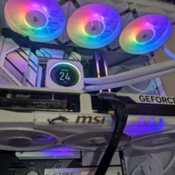 Wnętrze białej obudowy komputera stacjonarnego z podświetlanymi na tęczowo wentylatorami Corsair, kartą graficzną MSI GeForce RTX i chłodzeniem cieczą z wyświetlaczem temperatury.