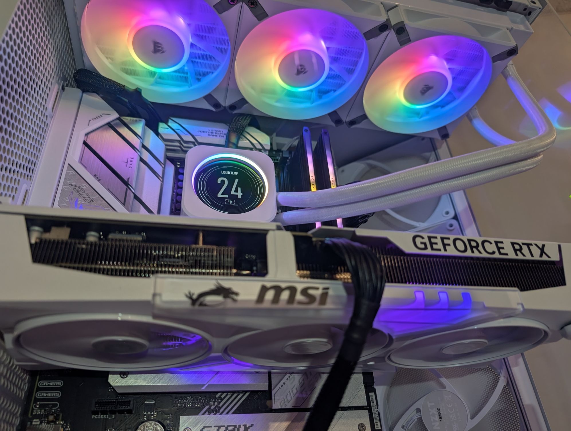 Wnętrze białej obudowy komputera stacjonarnego z podświetlanymi na tęczowo wentylatorami Corsair, kartą graficzną MSI GeForce RTX i chłodzeniem cieczą z wyświetlaczem temperatury.